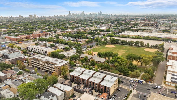 Panoramic aerial view of a city with residential buildings, green areas, and a distant city skyline.