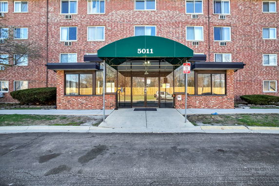Front view of a brick apartment building with a green awning entrance.