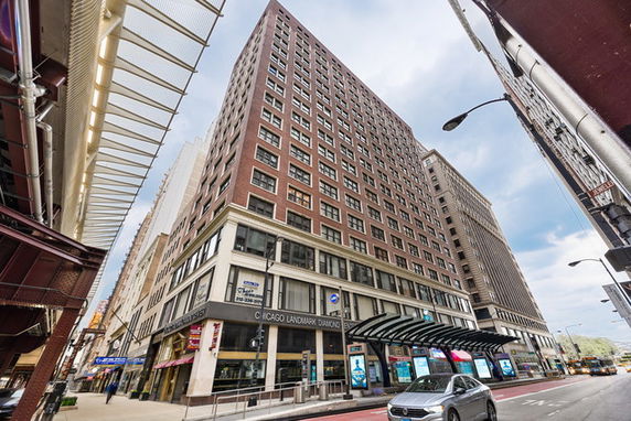 Front view of a tall, multi-story building with ground-level retail spaces and large windows.