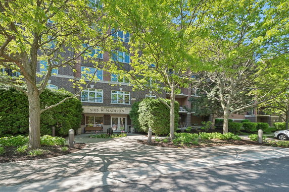 Front view of a mid-rise brick apartment building with large windows and greenery in front.