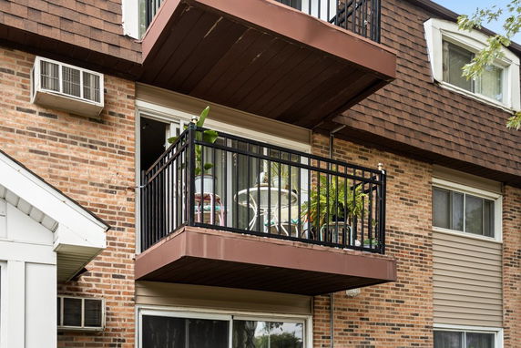 Front view of a brick apartment building with a balcony and window air conditioning unit.