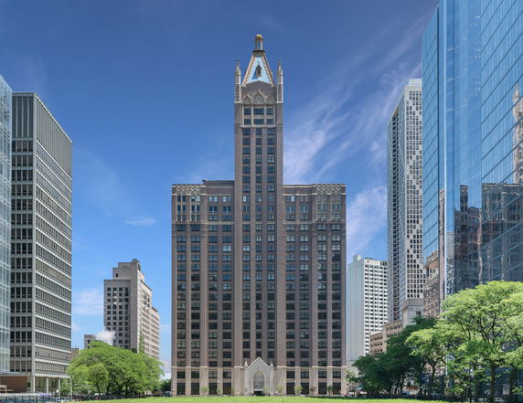 Front view of a tall skyscraper with a decorative top and large windows surrounded by other buildings.