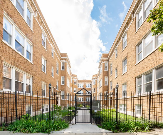 Front view of a brick apartment building with multiple windows and a gated entrance.