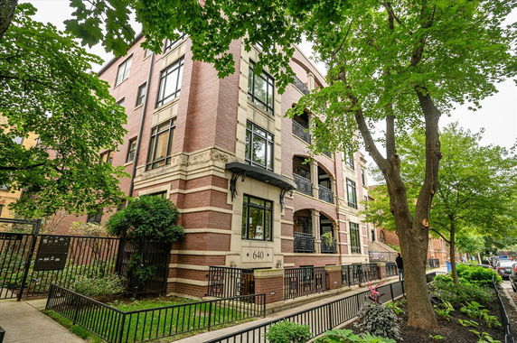 Front view of a multi-story brick building with balconies and a fenced entrance.