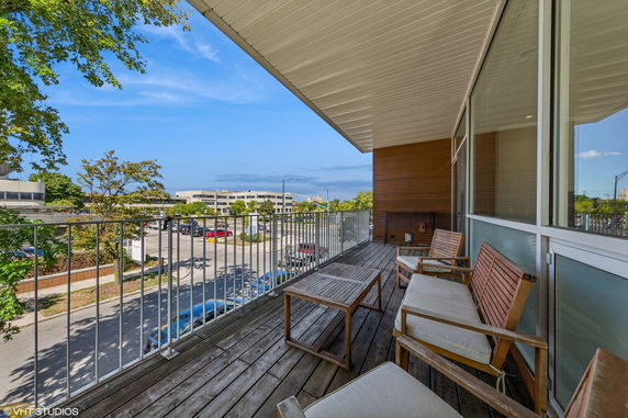 Panoramic view from a balcony with outdoor seating overlooking a street and buildings.