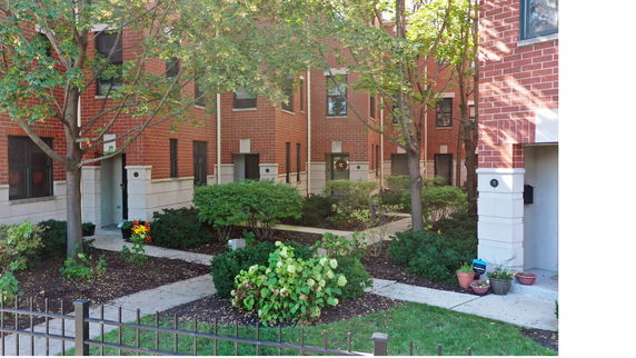 Front view of a two-story brick townhouse with multiple entrances and small garden areas.