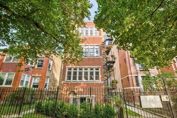 Front view of a multi-story brick building with large windows and a spiral staircase on one side.
