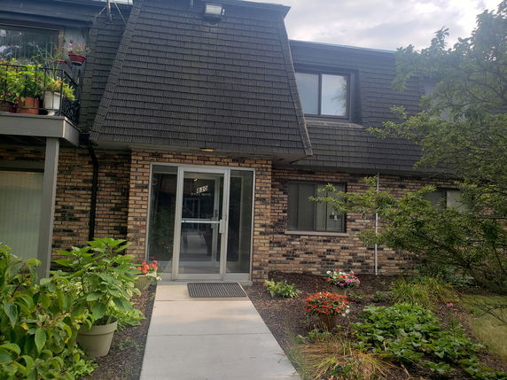 Front view of a brick building with a sloped shingle roof and entrance door.