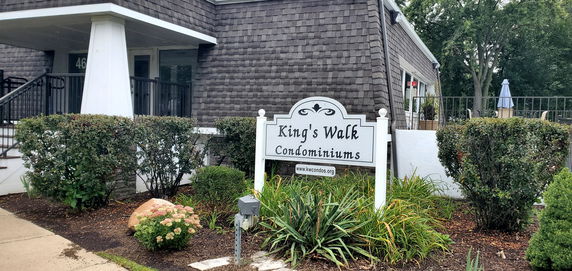 Front view of King's Walk Condominiums building with a sign and landscaped garden.