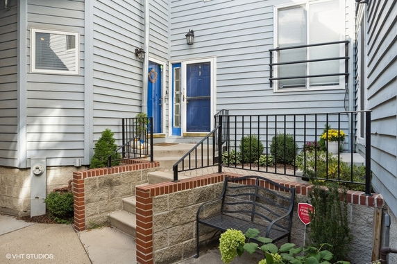 View of a residential building's entryway with steps, blue doors, and surrounding brick flowerbeds.