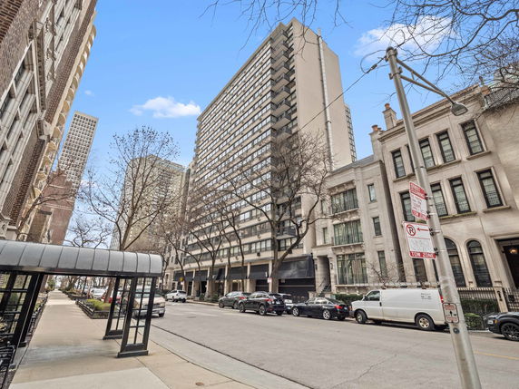 Street view of a tall residential building with multiple floors and large windows.