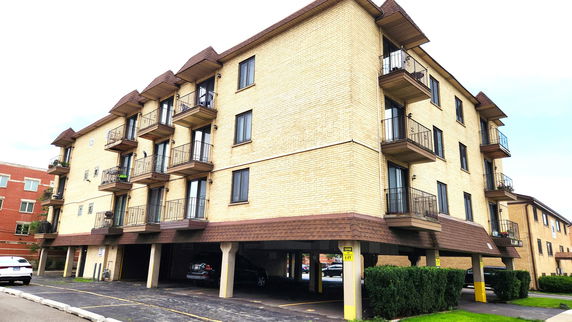 Front view of a multi-story apartment building with balconies and covered parking spaces.