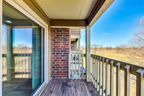 View of surrounding areas seen from a balcony, featuring a wooden railing and partial brick wall.