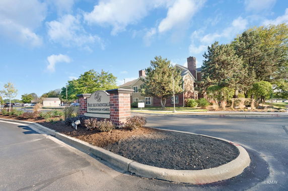 Front view of a condominium complex with a brick sign and surrounding greenery.