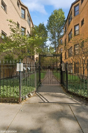 Entrance view of a gated apartment building with brick facade and walkway.
