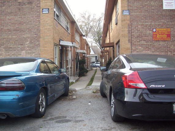 Outdoor parking area between two brick buildings with cars parked.