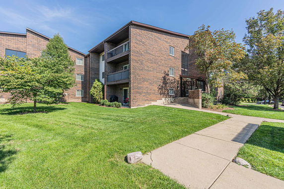 Front view of a multi-story brick apartment building with balconies and landscaped surroundings.
