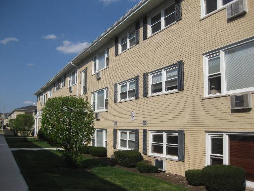 Front view of a multi-story brick apartment building with multiple windows and air conditioning units.
