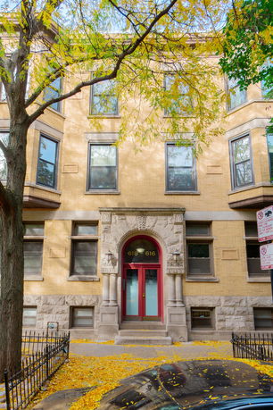 Front view of a three-story building with a distinctive stone entrance and red door.