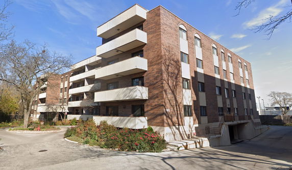 Front view of a multi-story brick apartment building with balconies and a driveway.