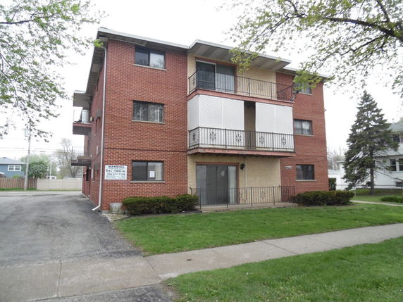 Front view of a three-story brick apartment building with balconies.
