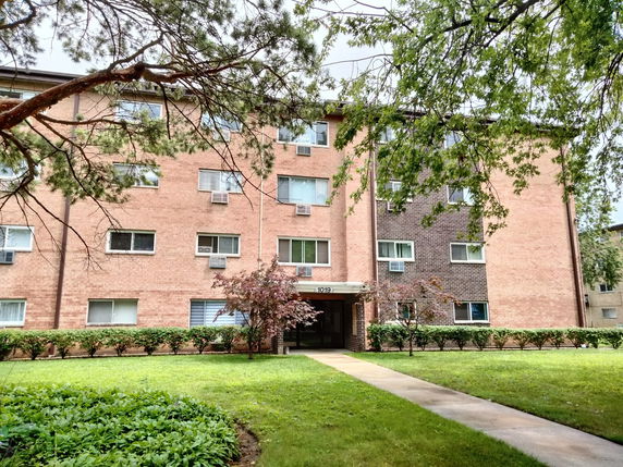 Front view of a multi-story brick apartment building with multiple windows and an entrance.