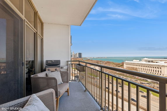 Balcony with chairs and a grill overlooking a cityscape and water body.