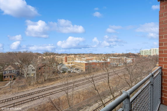 Panoramic view of residential and commercial buildings, railway tracks, and trees under a blue sky.
