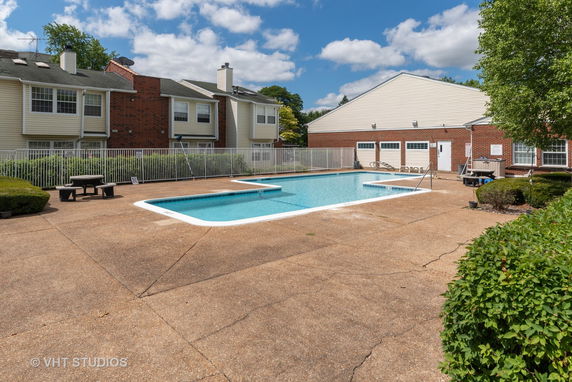 Outdoor swimming pool with a surrounding fence and residential buildings in the background.