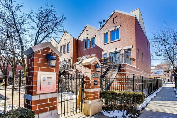 Front view of a three-story brick townhouse with a gated entrance and exterior staircases leading to the first floor.