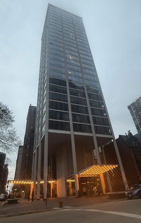 Front view of a tall modern building with large glass windows and illuminated entrance.