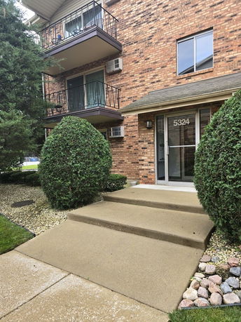Front view of a brick apartment building with balconies and a pathway leading to the entrance.