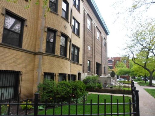 Side view of a multi-story brick building with windows and a fenced front garden.