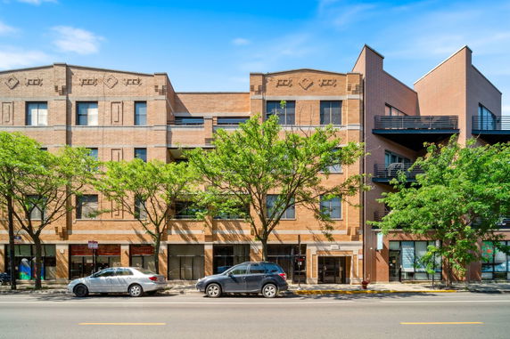 Front view of a multi-story brick building with trees and parked cars.