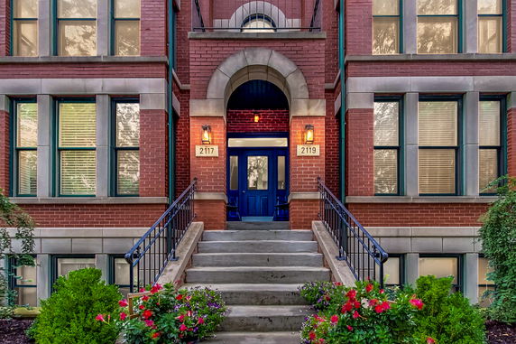Front view of a brick building entrance with steps and a blue door.