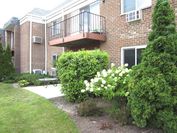 Front view of a brick residential building with balconies and shrubs.