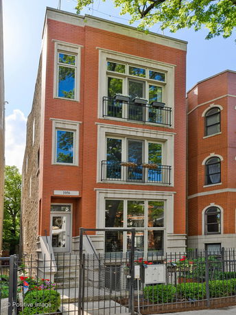 Front view of a three-story brick house with large windows and balconies.