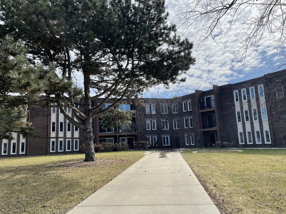 Front view of a multi-story building with large windows and a walkway leading to its entrance.