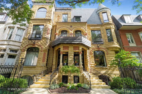 Front view of a three-story stone house with arched windows and ornate balconies.