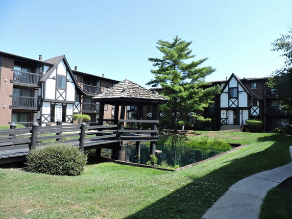 Front view of apartment buildings with Tudor-style architecture and a small pond with a wooden bridge.