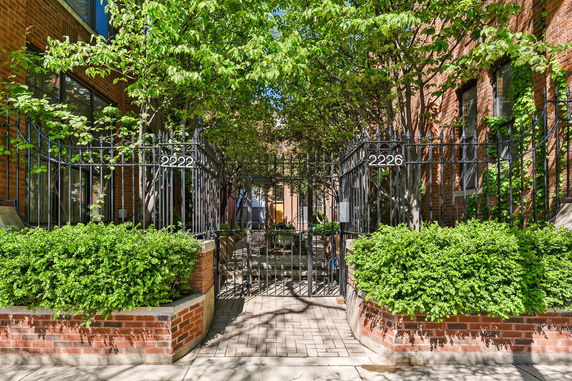 Front view of a brick building with decorative iron fencing and greenery.