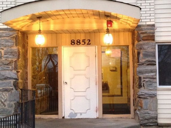 Front view of a building entrance with a white door and illuminated lamps.