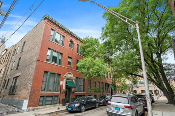 Front view of a multi-story brick building with green window frames and an arched entrance.