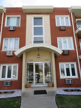 Front view of a multi-story brick apartment building with a central entrance.