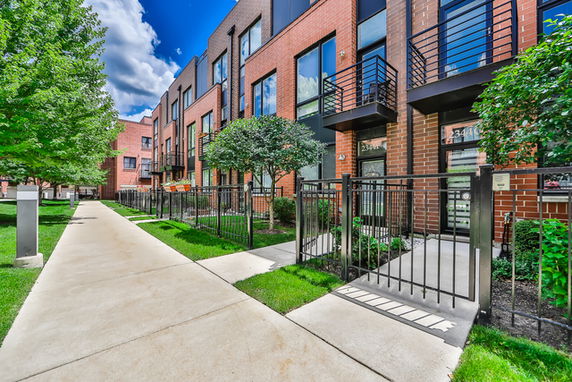 Front view of a row of modern townhouses with brick exteriors and small fenced front yards.