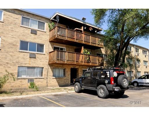 Front view of a multi-story apartment building with wooden balconies and parking area in front.