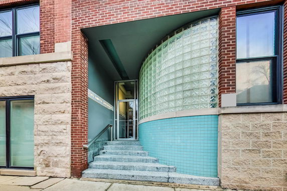 Front view of a building entrance with curved glass block wall and stairs leading to the door.