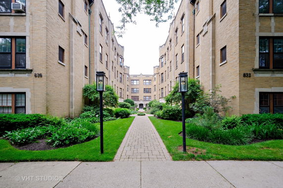 Front view of a multi-story brick apartment building with a walkway and garden.