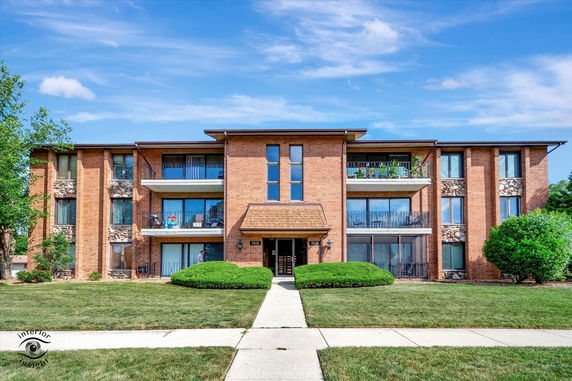 Front view of a three-story brick apartment building with balconies.