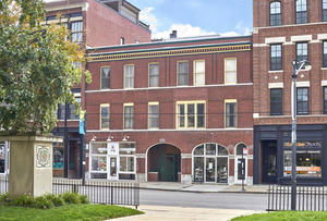 Front view of a three-story building with brick facade and arched windows on the ground floor.
